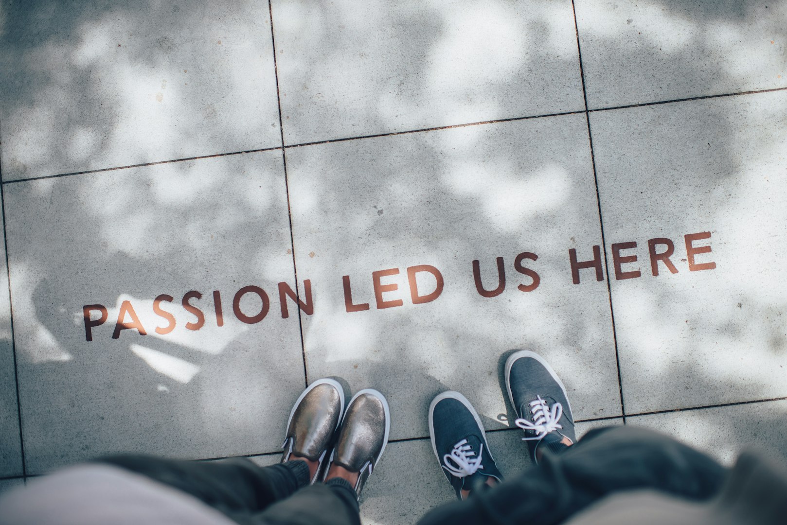 Två personer står och tittar ner på texten 'Passion Lead Us Here' tryckt på marken.